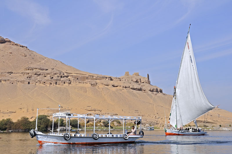 Faluka and motorboat passing by tombs on bank of the Nile near Aswan